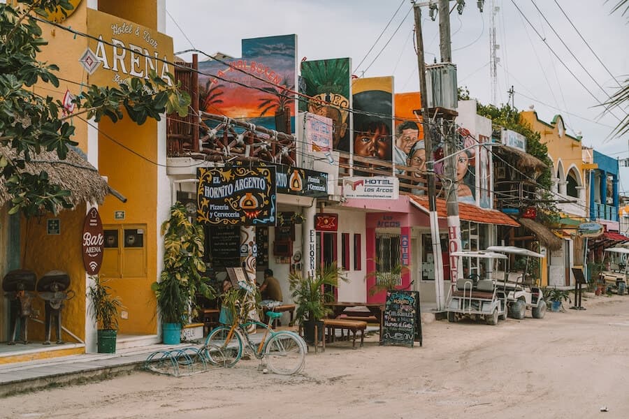 Colorful hand-painted shopfronts along a sandy street in Tulum